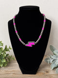 A beaded necklace displayed on a black velvet jewelry bust. The necklace features gray metallic beads with bright pink accent beads and a central pink lightning bolt charm outlined with small silver beads.